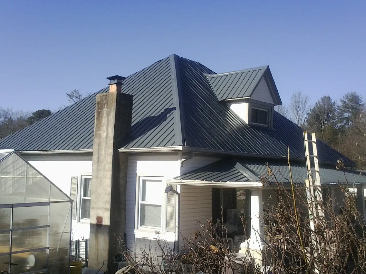 Dark blue standing seam metal roof on a white farmhouse with dormer — Slate & Tile Roof Repair by Roofing Brothers in Columbiaville