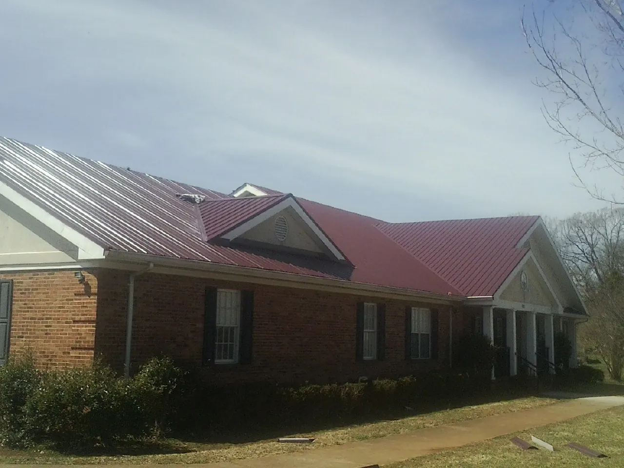 Red metal roof with gabled entries on a long brick building, from a Hail Damage Roof Repair job in Columbiaville