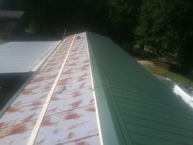 Old rusted panels beside newly installed green metal roofing — Wind Damage Roof Repair by Roofing Brothers in Columbiaville