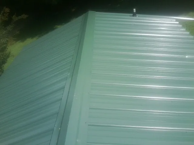 New green metal panels meeting at the ridge of a roof — Flat Roof Repair work by our crew in Columbiaville