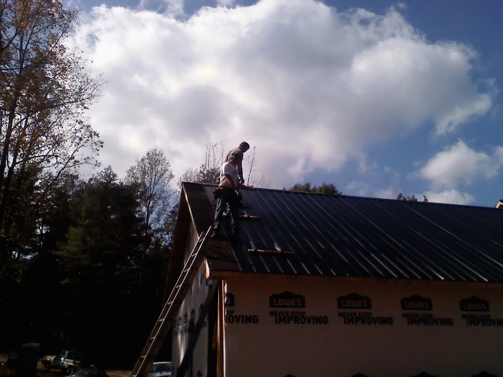 Roofer fastening dark metal panels high against a cloudy sky, from a Roof Inspection job in Columbiaville