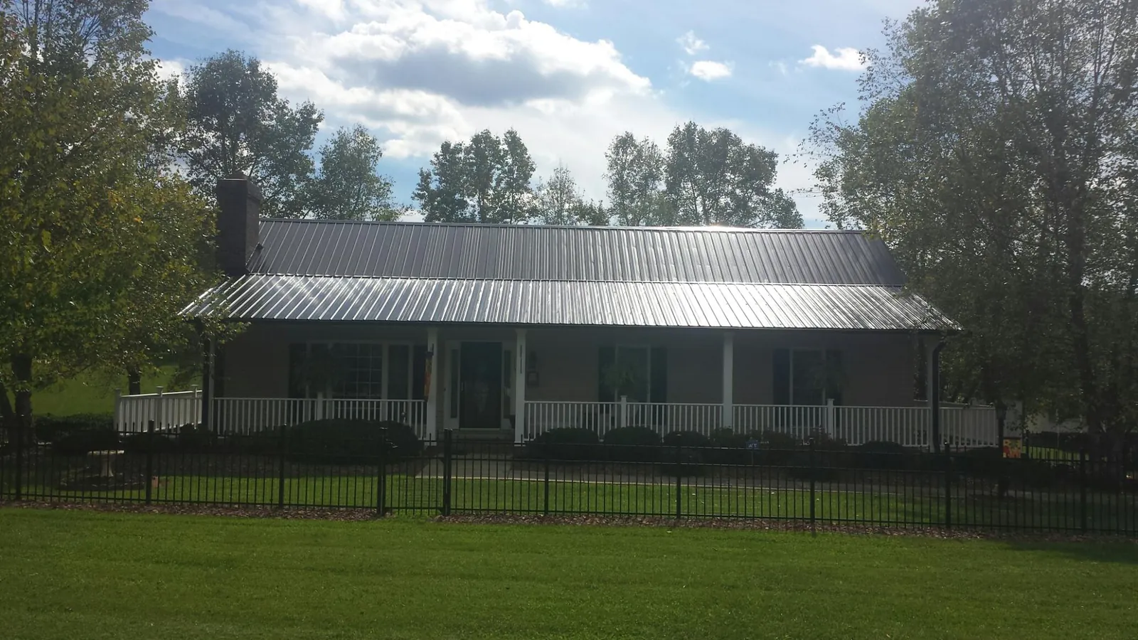 Gray metal roof on a brick ranch with a full width front porch — Gutter Guard Installation work by our crew in Columbiaville
