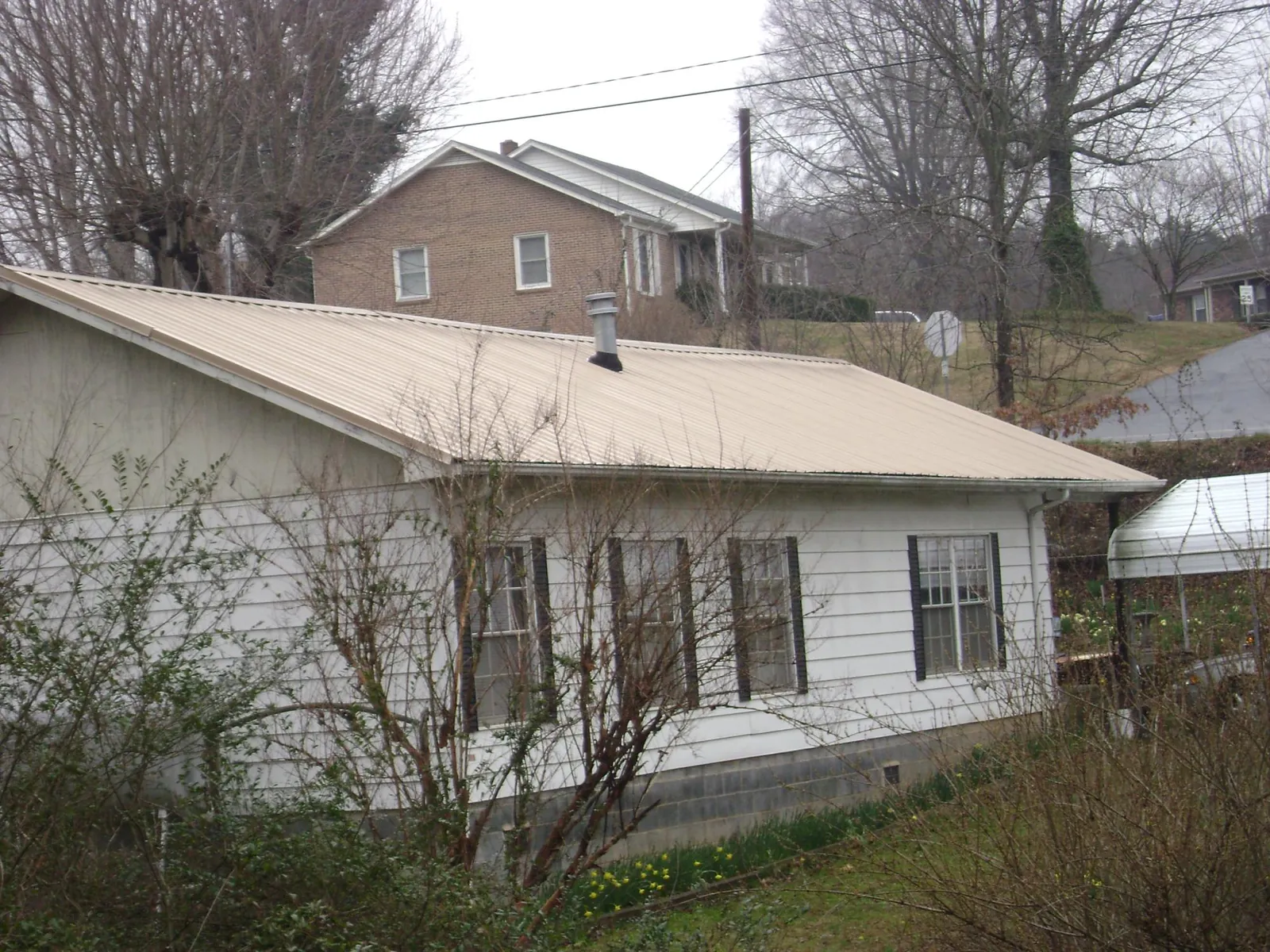 Tan metal roof on a white sided house set into a hillside — Commercial Roofing by Roofing Brothers in Columbiaville
