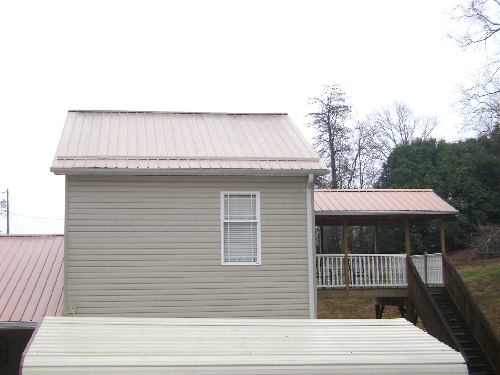 Tan metal roofs on a two story addition and attached porch, from a Roof Replacement job in Columbiaville