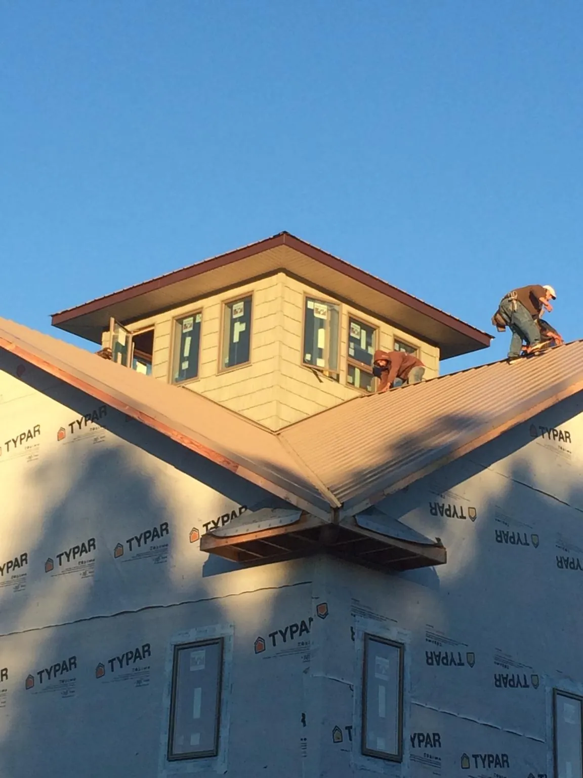Roofers working around a rooftop cupola on a new metal roof at sunset — Roof Waterproofing in Columbiaville by Roofing Brothers